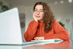 Young student using a laptop at a desk, whilst taking notes in a notebook