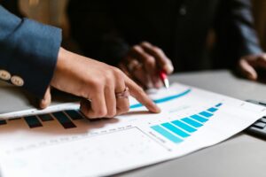 Two people's hands pointing at a blue graph on a white piece of paper